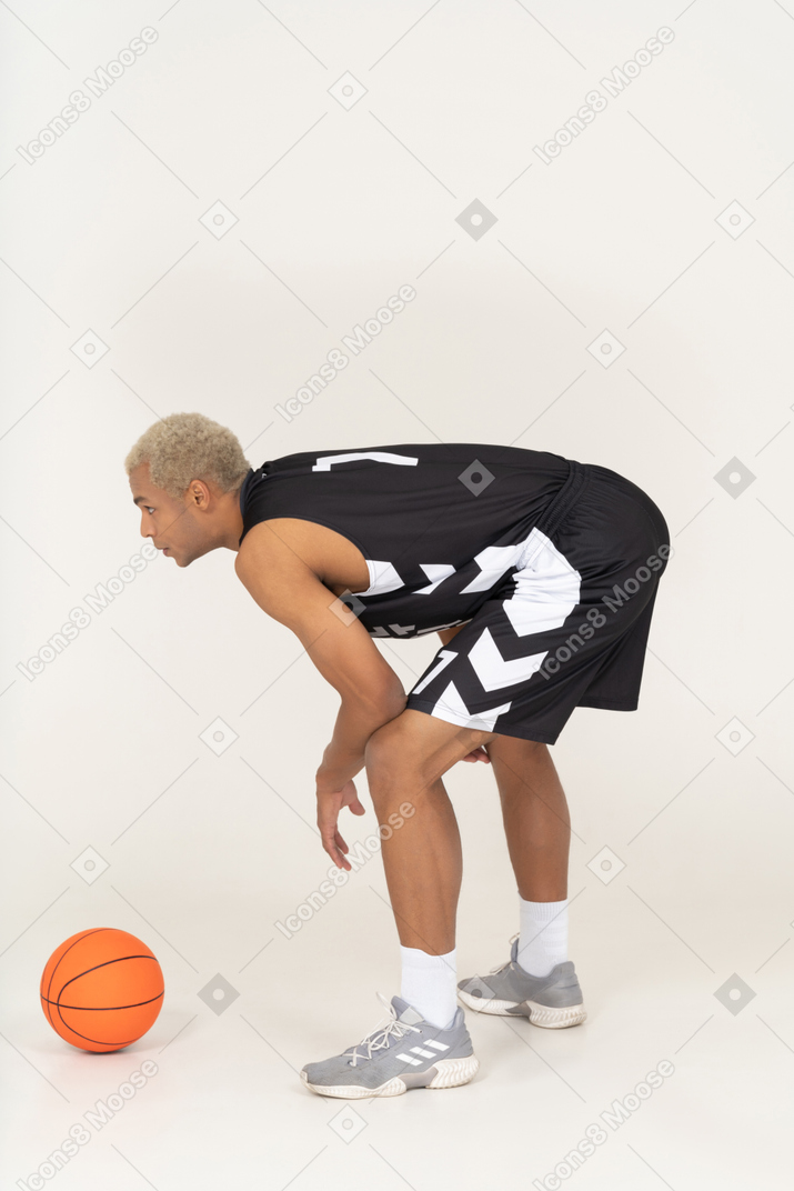 Vista laterale di un giovane giocatore di basket maschile in piedi vicino alla palla