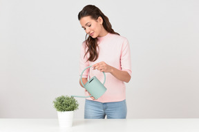 Attraente giovane donna innaffiando una pianta d'appartamento