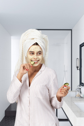 Chica con el pelo envuelto en una toalla y máscara en su cara con rodajas de pepino