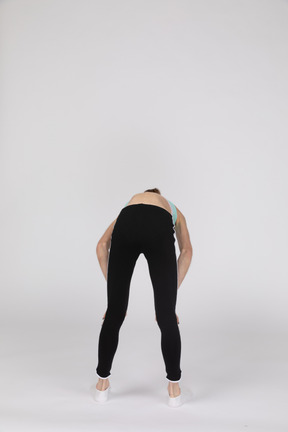 Side view of a teen girl in sportswear squatting and putting hands on hips