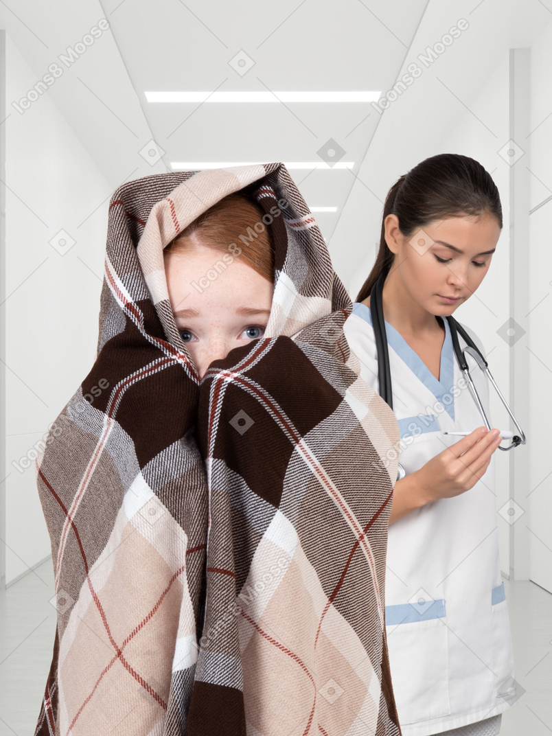 Uma criança em um cobertor e uma enfermeira com um termômetro
