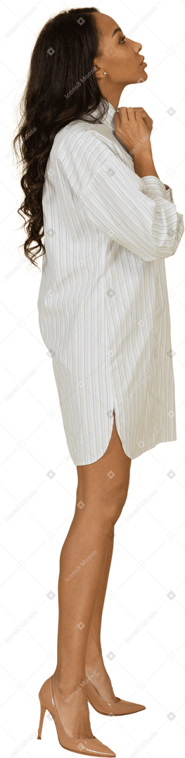 Vista lateral de uma jovem mulher de pele escura em um vestido branco ajustando o colarinho