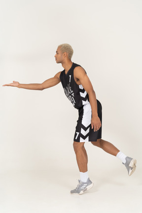 Vista laterale di un giovane giocatore di basket maschile che tende la mano
