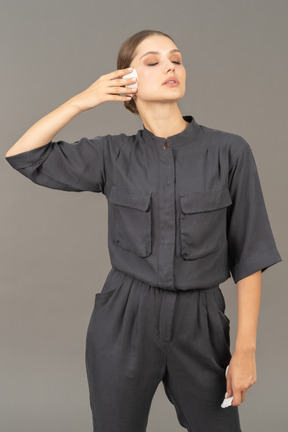 Front view of a young woman in a jumpsuit removing make-up