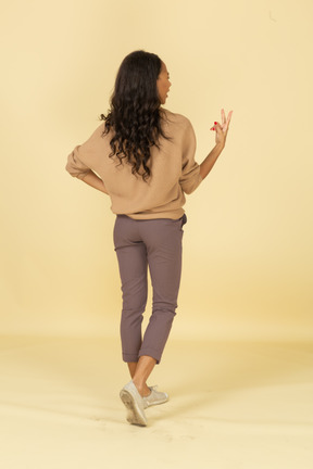 Вид сзади в три четверти темнокожей молодой женщины с двумя пальцами