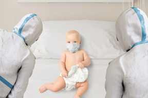 보호 장비를 입은 의사들에게 둘러싸인 병원 침대에 누워 있는 아기