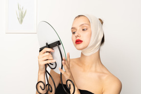 Young woman with head bandage holding a mirror