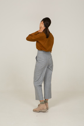 Vista posteriore di una giovane donna asiatica in calzoni e camicetta che tocca il collo