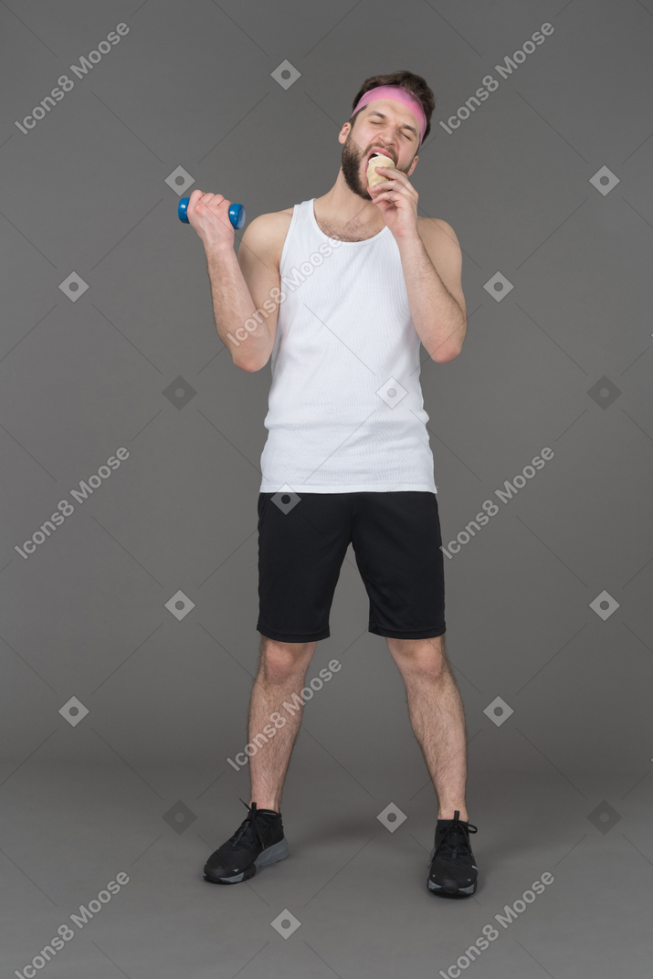 Мужчина держит гантели и ест мороженое