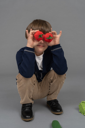 Niño sosteniendo dos tomates frente a sus ojos mientras se pone en cuclillas