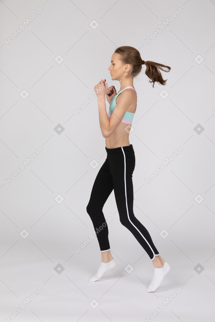 Side view of a teen girl in sportswear stepping forward while clenching fists