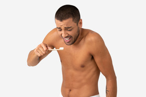 Barechested young man brushing his teeth with disgusted expression