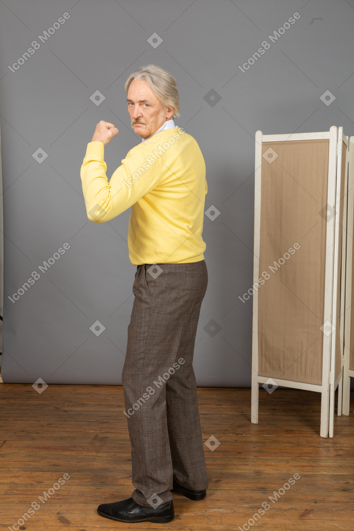Side view of an old man looking at camera while demonstrating his strength