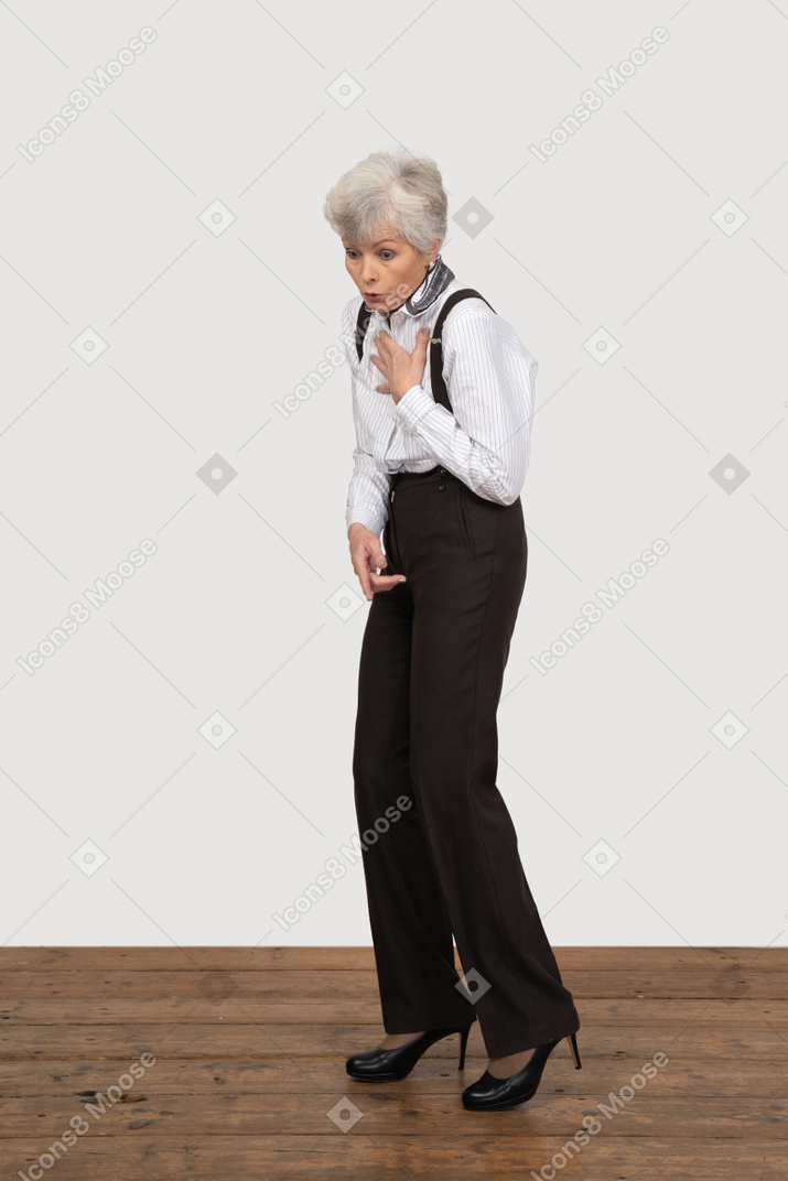 Three-quarter view of an astonished old lady in office clothing touching her chest