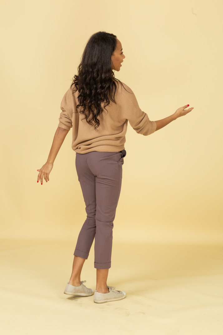 Three-quarter back view of a dark-skinned young female outstretching her hand