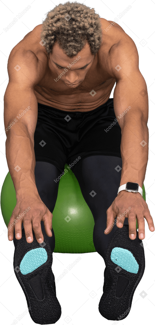 Vista frontal de um homem afro sem camisa se alongando sentado em uma bola de ginástica verde