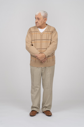 Front view of an old man in casual clothes standing with crossed hands and looking aside
