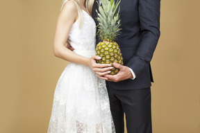 Braut und bräutigam, die eine ananas umarmen und halten