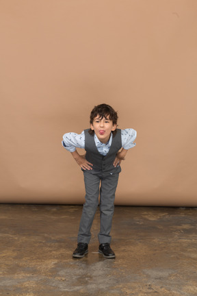 Vista frontale di un ragazzo in giacca e cravatta in piedi con le mani sui fianchi e chinandosi