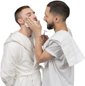 A man putting a shaving foam on his boyfriend's face