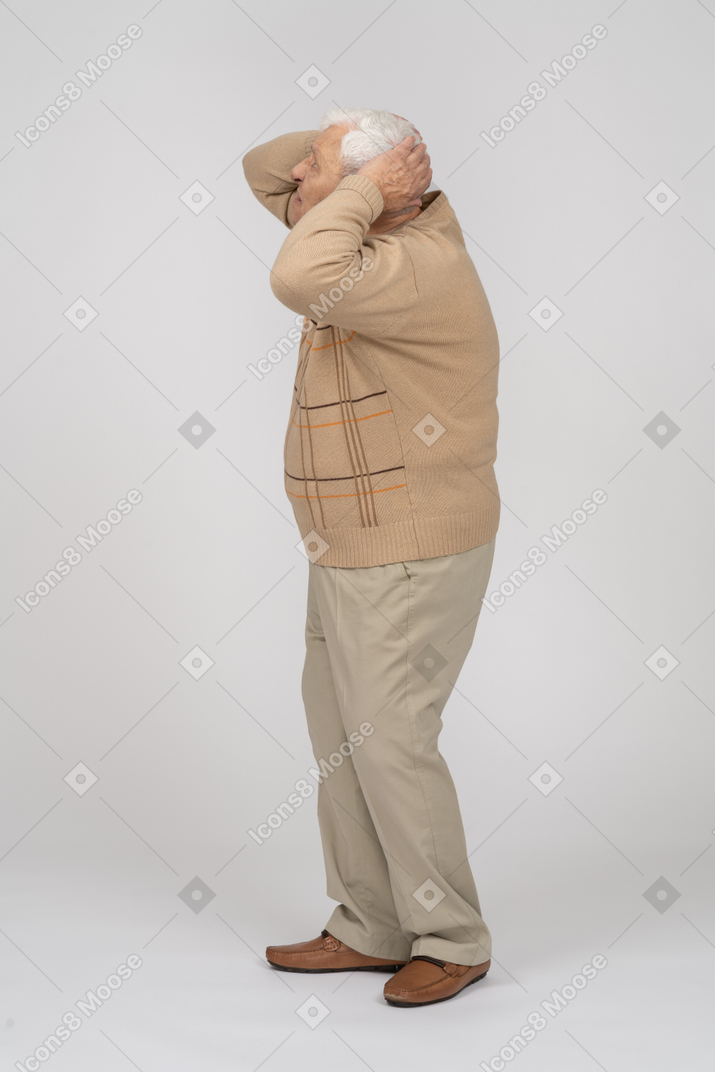 Side view of a sad old man standing with hands behind head
