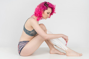 Young woman with curly pink hair shaving legs