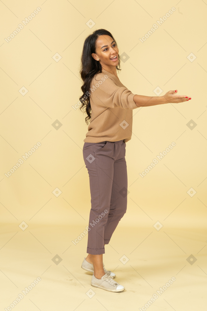 Vista de tres cuartos de una mujer joven de piel oscura extendiendo su mano