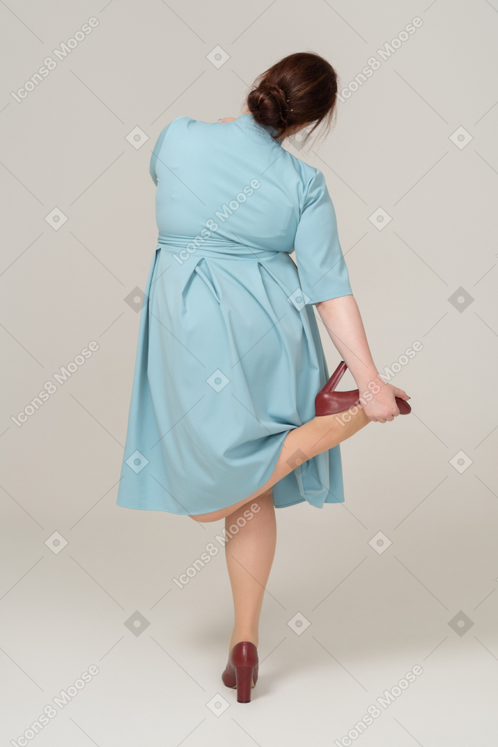 Женщина в синем платье балансирует на одной ноге, вид сзади