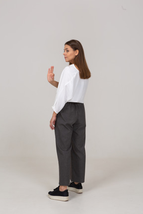 Vista posterior de tres cuartos de una joven en ropa de oficina mostrando gesto ok