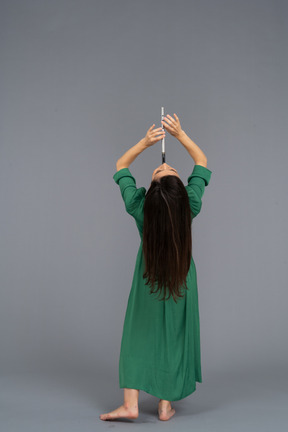 Back view of a young lady in green dress playing flute while leaning back