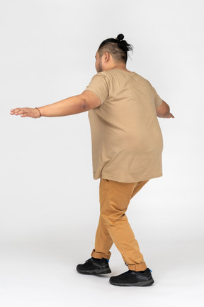 Plump black haired man imitating balancing