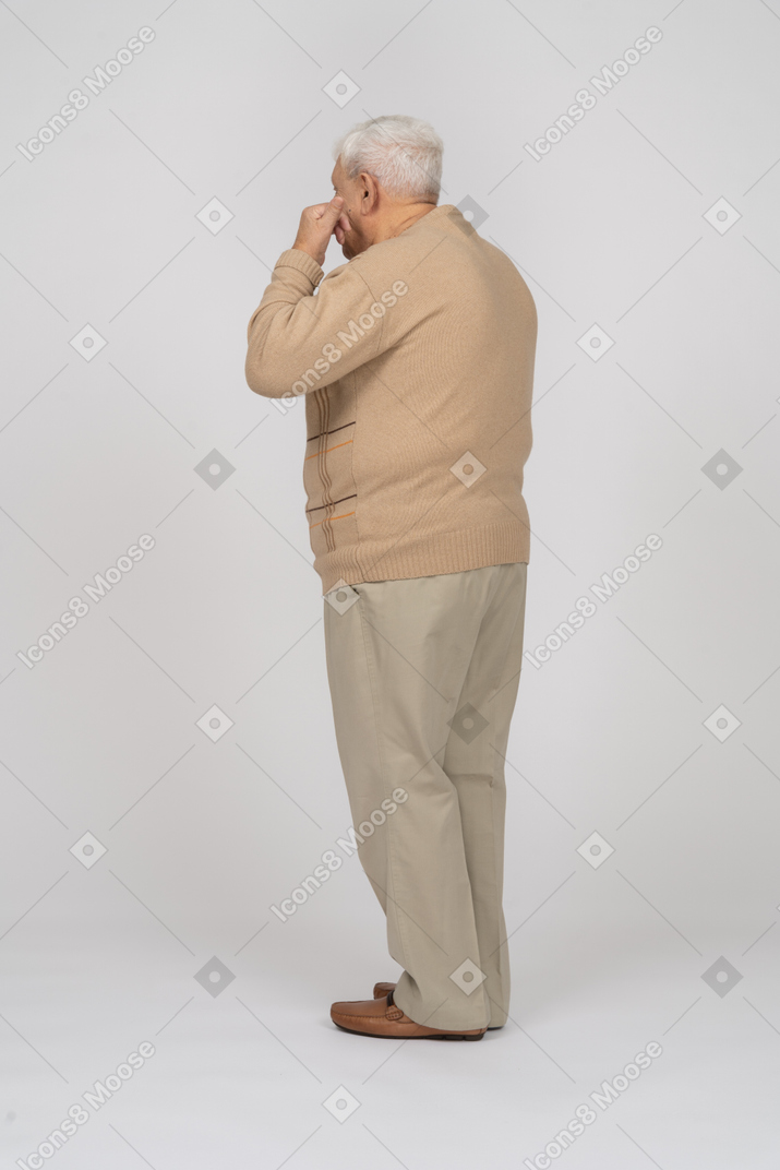 Side view of an old man in casual clothes touching face