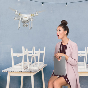 Surprised woman with laptop sitting on chair and looking at drone