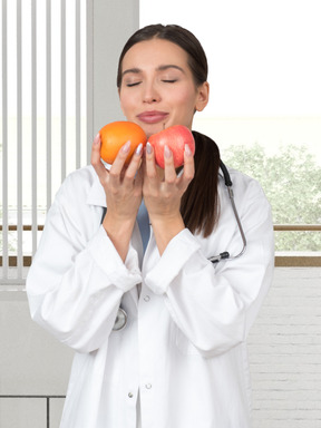 A woman in a white lab coat holding an apple and an orange
