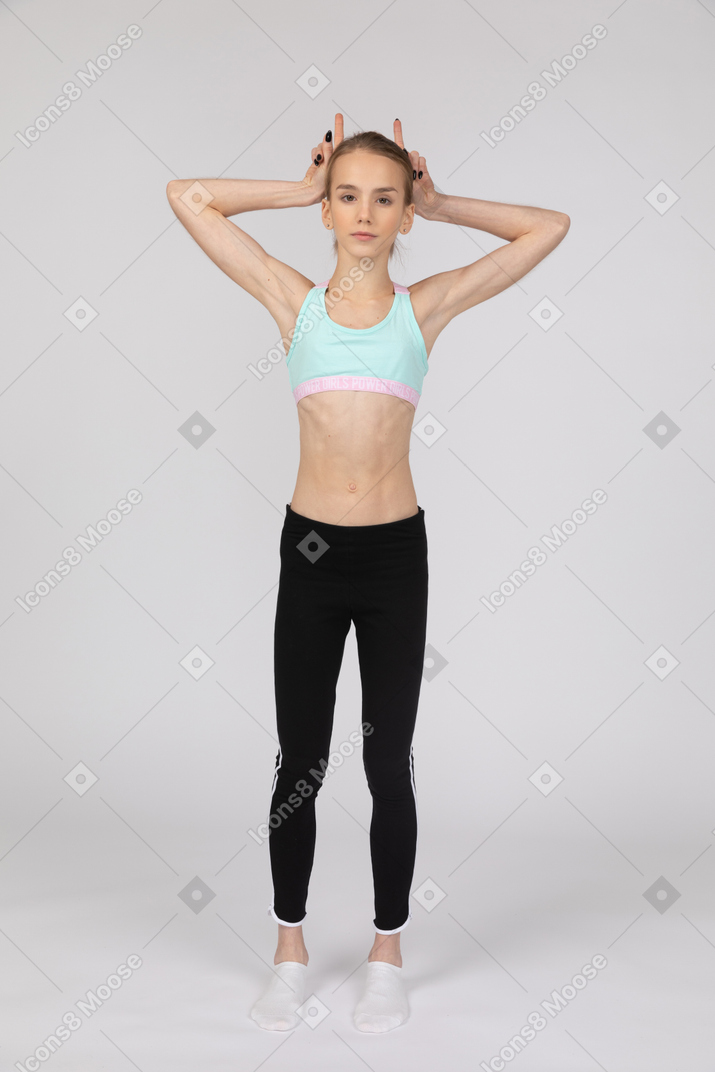 Front view of a teen girl in sportswear making horns
