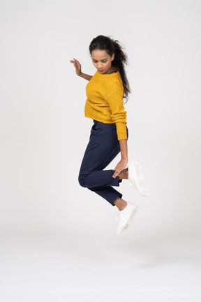 Vista lateral de uma garota com roupas casuais pulando e tocando o pé