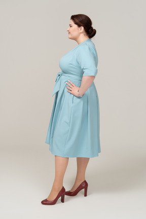 Vue latérale d'une femme en robe bleue posant avec les mains sur les hanches