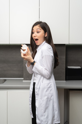 Gros plan d'une femme dentiste surprise tenant un prototype de mâchoires et regardant de côté
