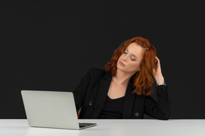 Beautiful red haired girl sitting at the table with laptop and touching her hair