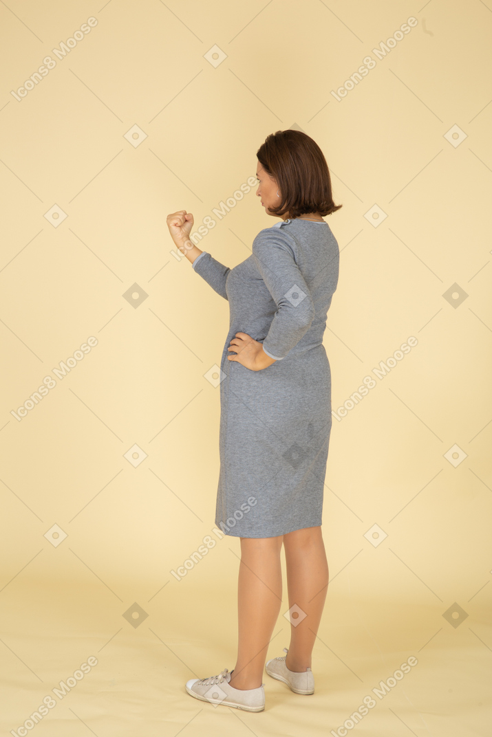 Vista posteriore di una donna in abito grigio che minaccia qualcuno con un pugno