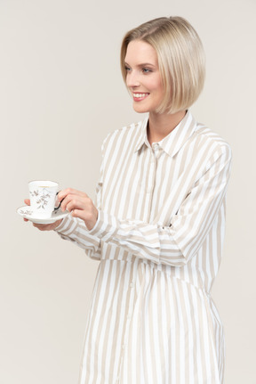 Smiling young woman standing half sideways and holding cup of tea