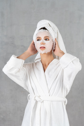 Woman in bathrobe with face mask on holding head