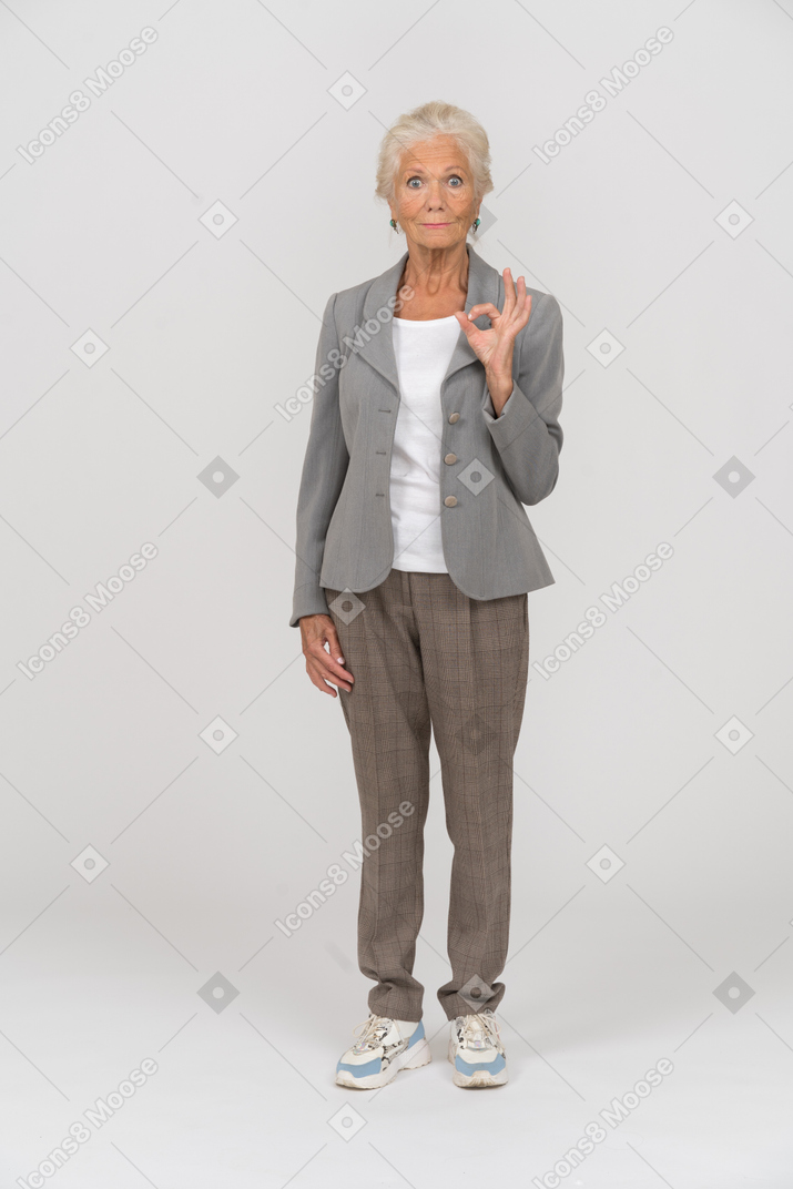 Vista frontal de uma senhora idosa de terno mostrando sinal de ok