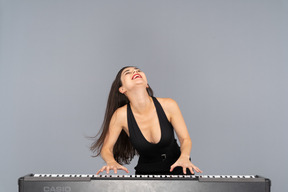 Front view of a young lady in black dress enjoying playing the piano