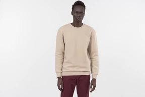 Un joven negro en un suéter gris de pie solo sobre el fondo blanco.