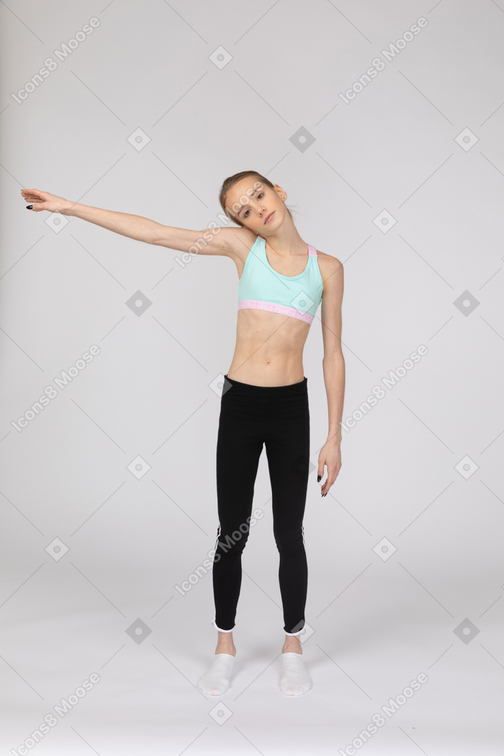 Vista frontal de uma adolescente em roupas esportivas estendendo a mão e inclinando a cabeça