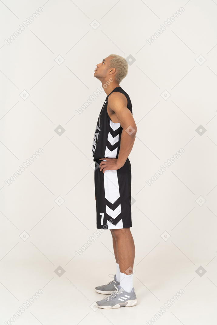 一个年轻的男篮球运动员把手放在臀部上仰望的侧视图