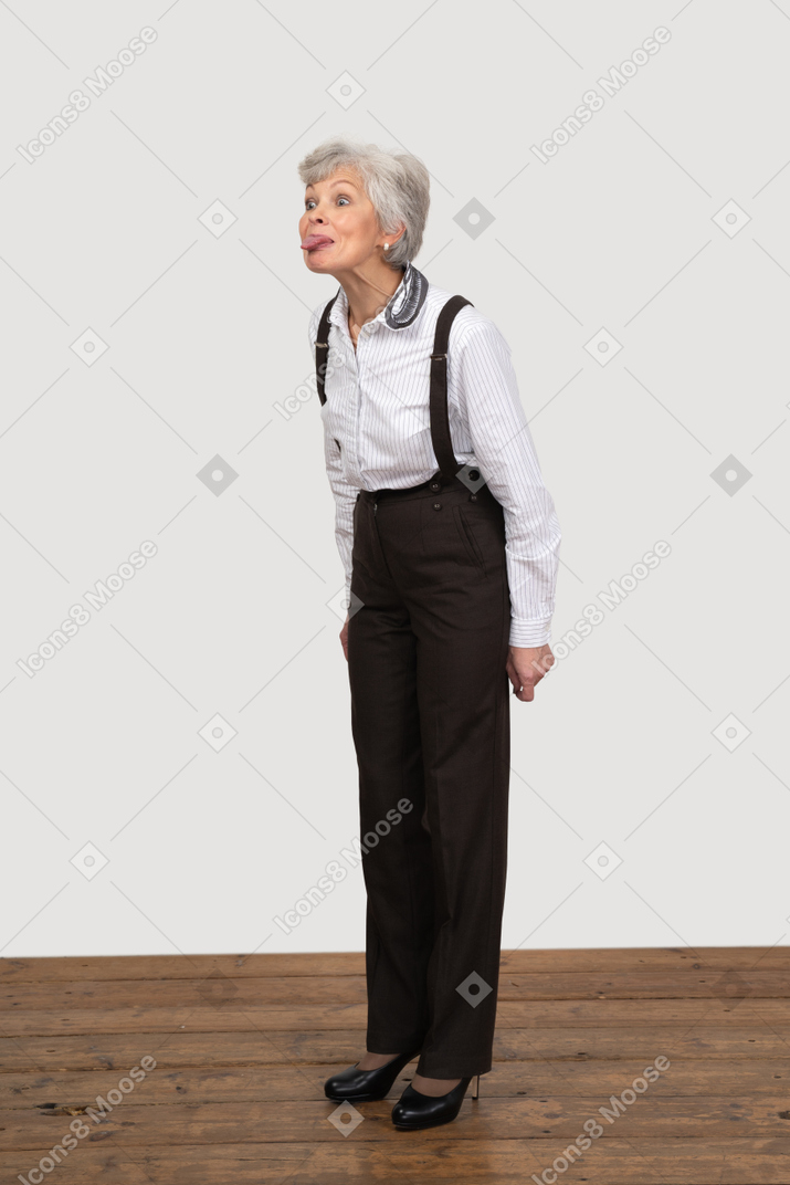 Vista de tres cuartos de una anciana burlona en ropa de oficina mostrando la lengua
