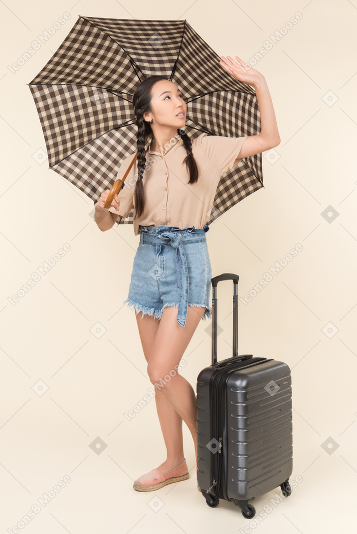 여행 가방과 우산으로 얼굴을 가리고 있는 젊은 여성