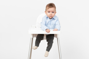 Прелестный маленький мальчик сидит в стульчике